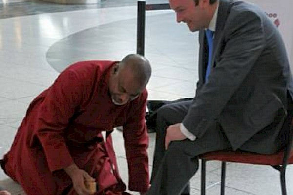 The Dean shines the shoes of David Allinson, Centre Director of Manchester Arndale